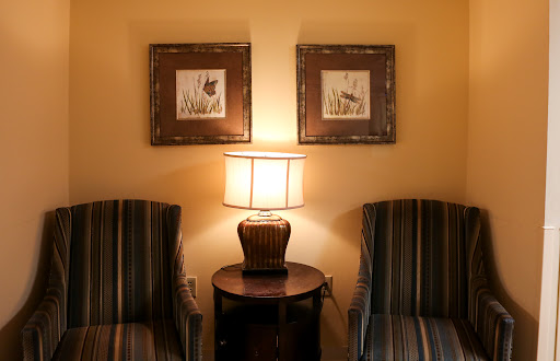 A cozy corner of a living room featuring two striped chairs, a lamp on a side table, and framed artwork on the wall.