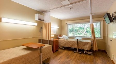 A hospital room with two beds, curtains, and an air conditioning unit.