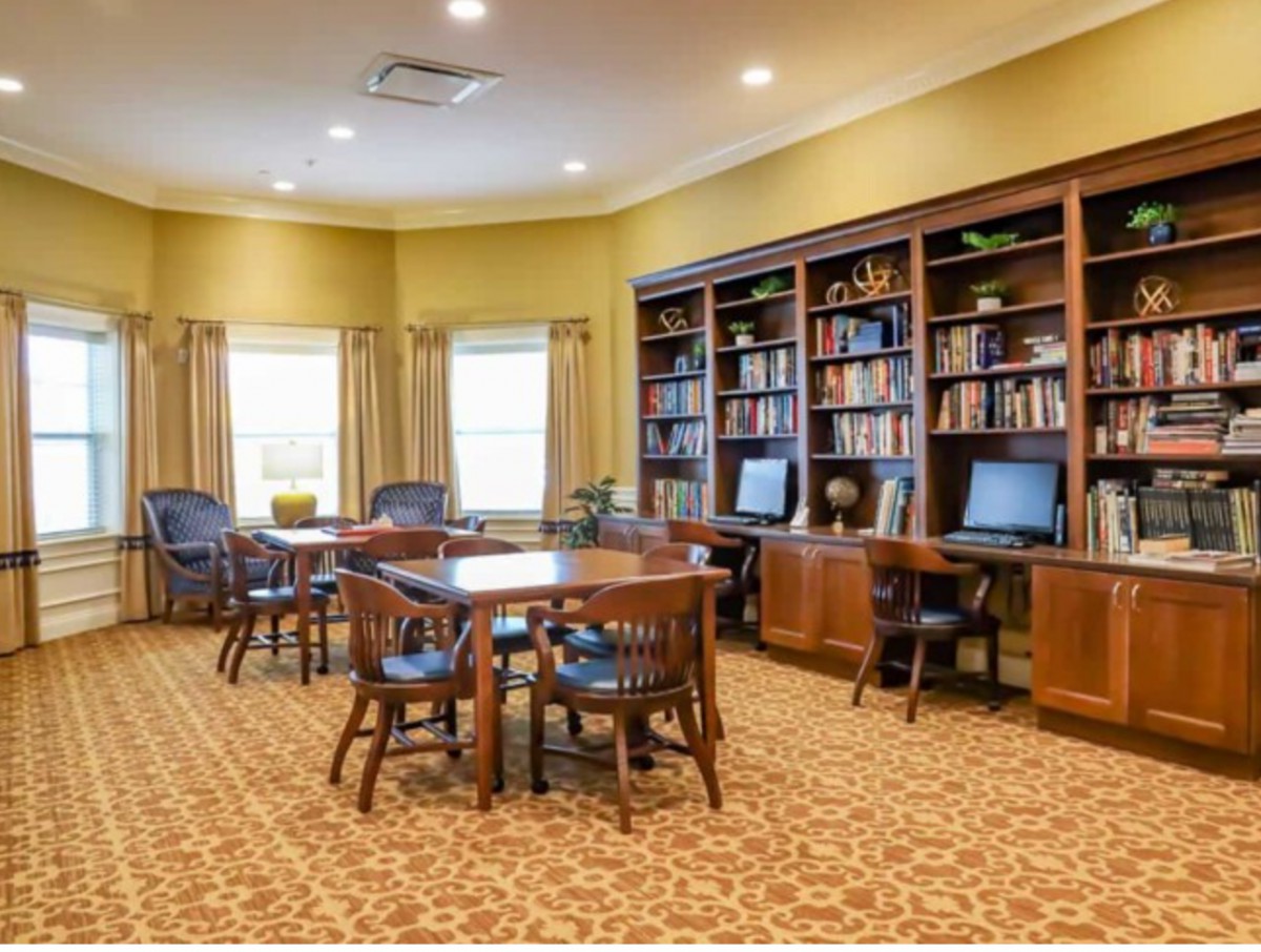 A cozy library with bookshelves, tables, chairs, and computers.