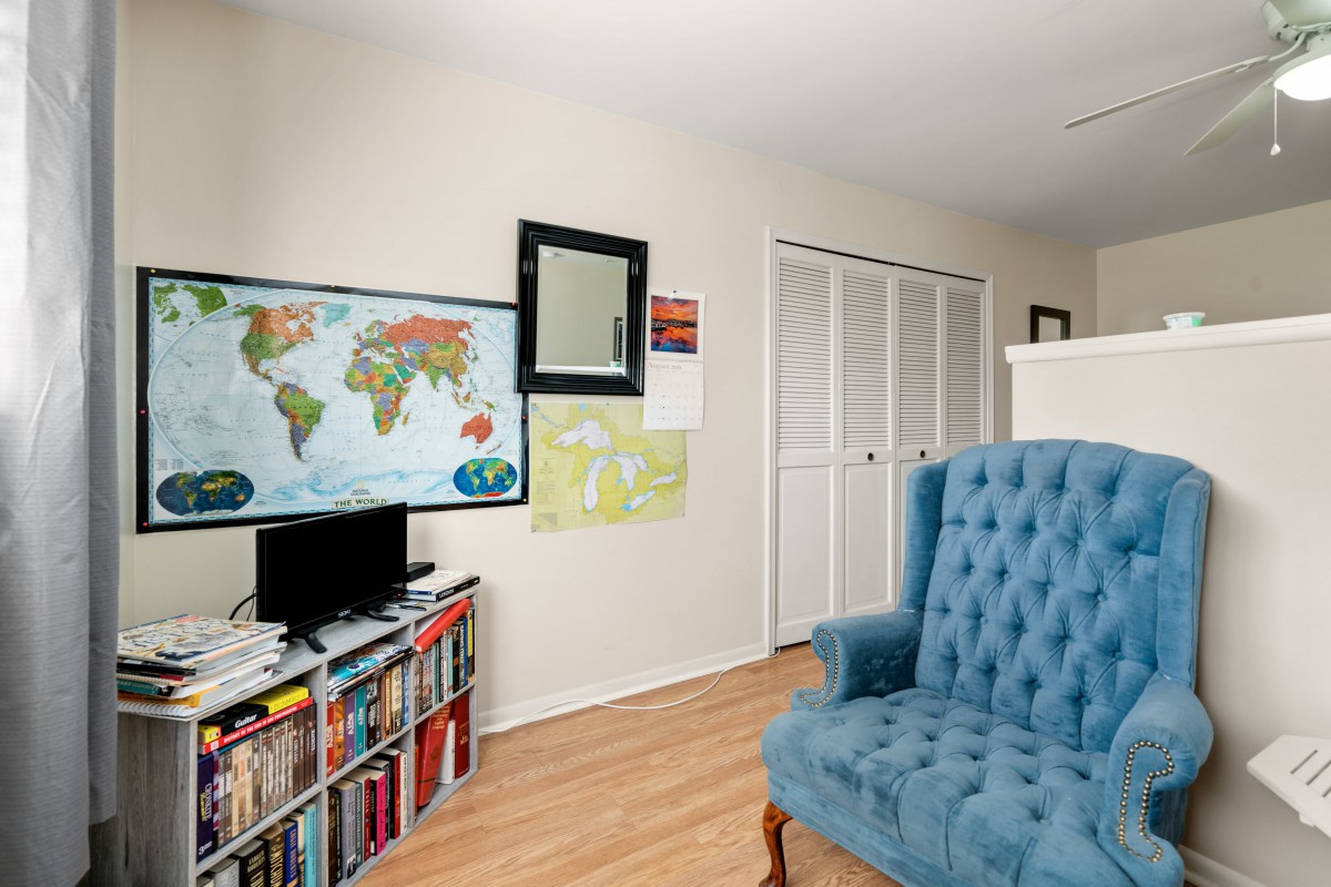 A cozy living room with a blue armchair, a bookshelf filled with books, and a world map on the wall.