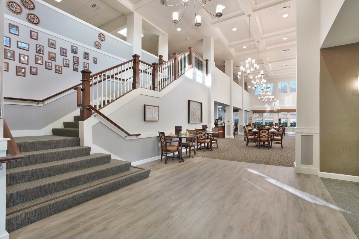 A spacious and elegantly designed lobby area featuring a staircase, chandeliers, and comfortable seating.