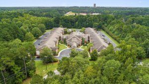 Aerial view of residential buildings surrounded by dense forest and greenery in a suburban area.