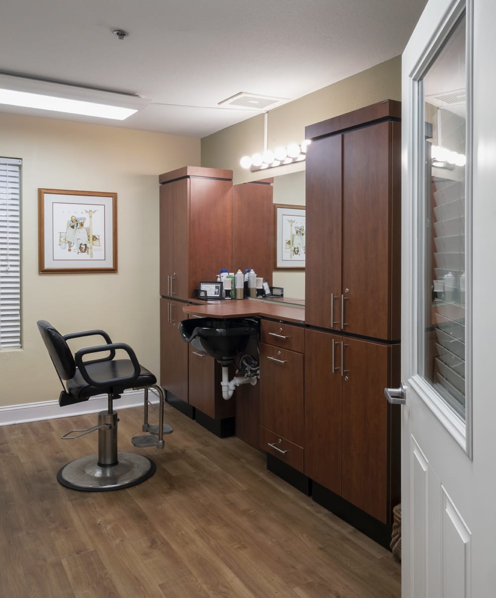 A modern hair salon interior with a styling chair, mirror, and wooden cabinets.