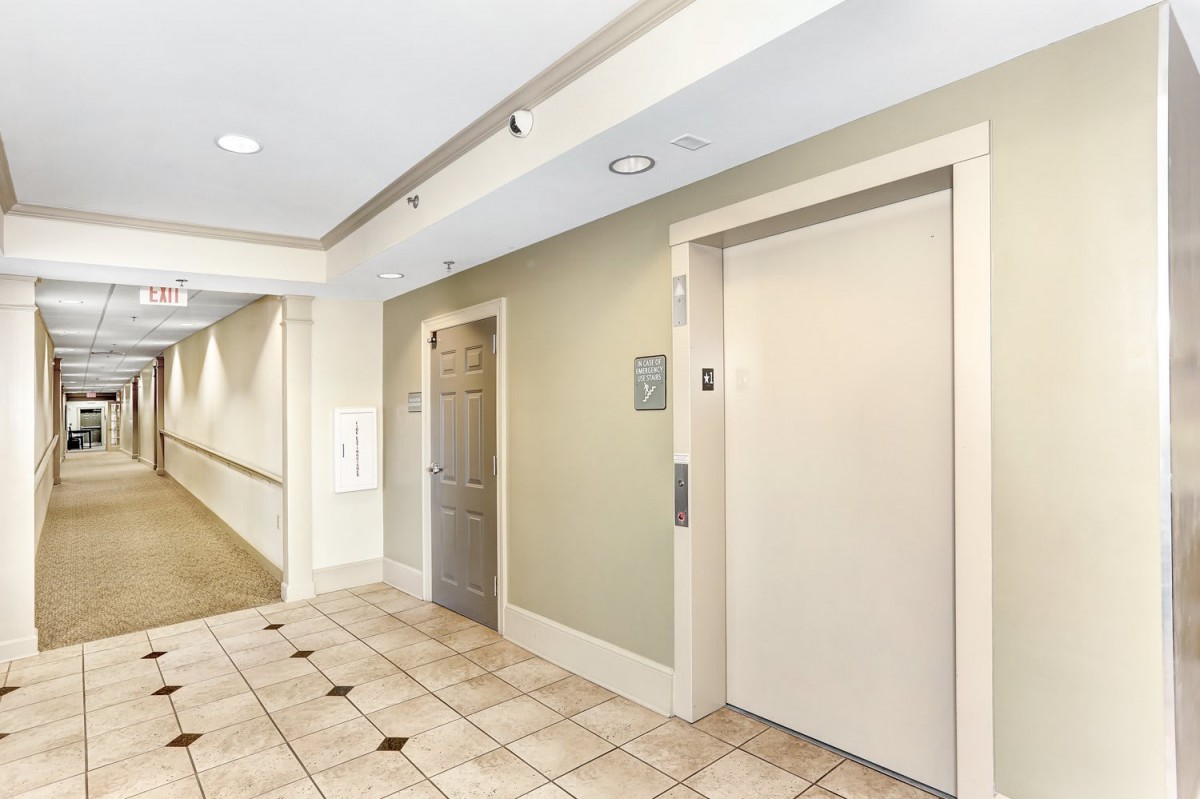 A well-lit hallway with an elevator and a side door, featuring tiled flooring.