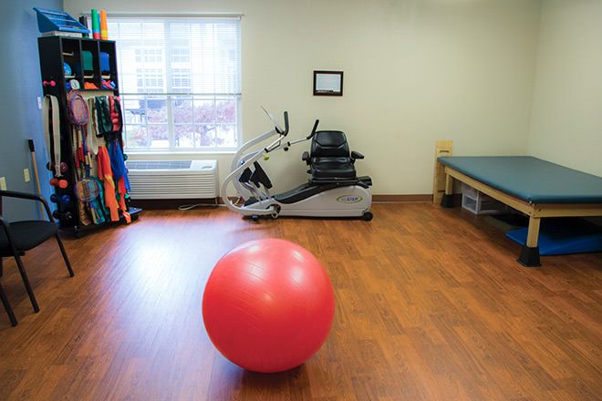 A therapy room with a recumbent bicycle and a large red exercise ball.