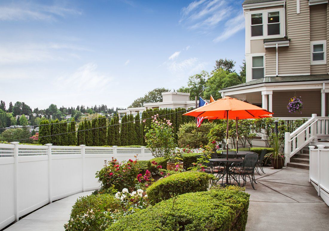 A beautiful garden patio with colorful flowers and an orange umbrella, providing a cozy outdoor seating area next to a house.