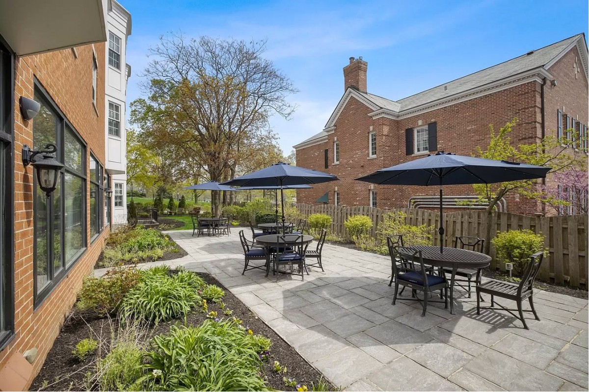 A sunny outdoor patio with tables, chairs, and umbrellas next to a brick building.