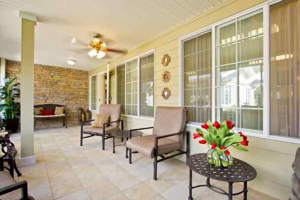 A bright and inviting patio area with comfortable chairs, a table adorned with tulips, large windows, and a ceiling fan.