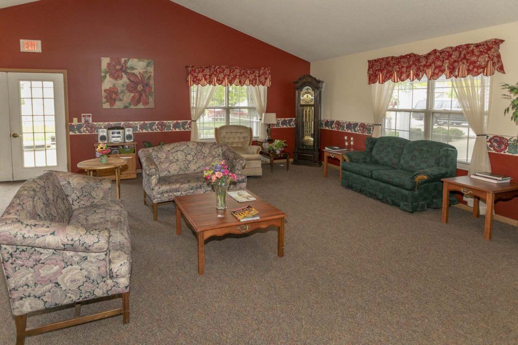 A cozy living room with comfortable sofas, a wooden coffee table, and a grandfather clock against red walls.