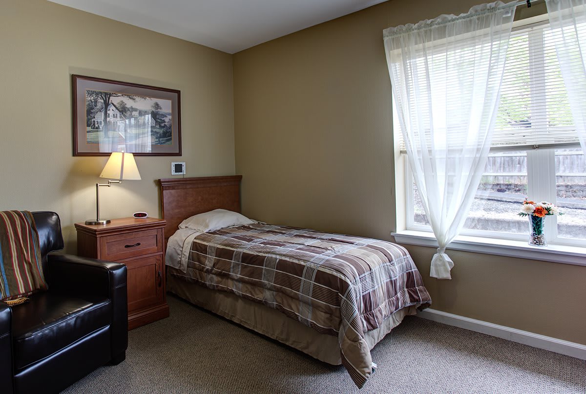 A cozy bedroom with a single bed, nightstand, and window with curtains.