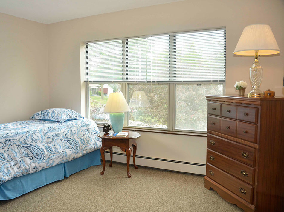A cozy bedroom with a bed, dresser, and a window letting in natural light.
