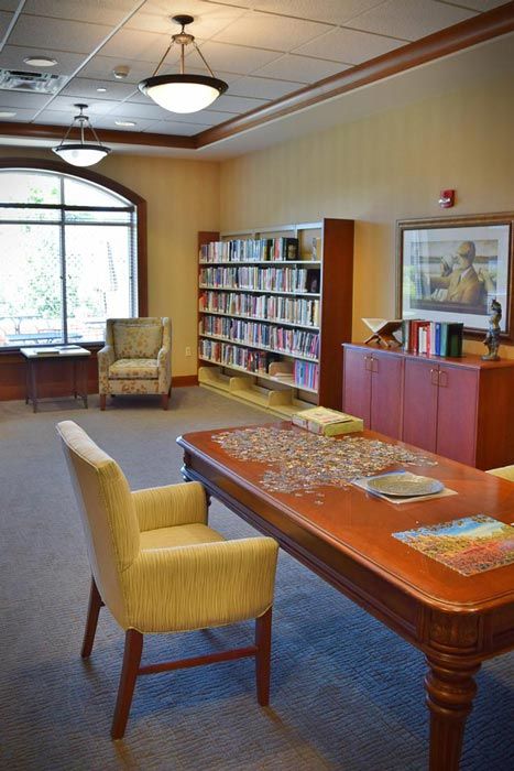 A cozy library room with bookshelves, a table with a puzzle, and comfortable seating.