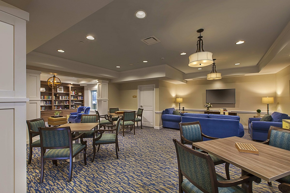 A cozy lounge area with tables, chairs, and bookshelves, complemented by sofas and a television.