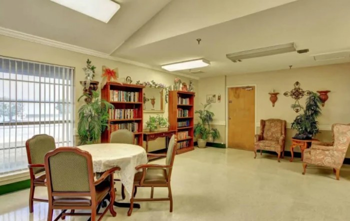 A cozy library reading room with bookshelves, a table, and comfortable chairs.