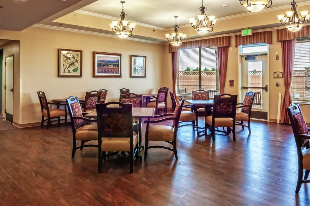 A spacious dining area with elegant chandeliers, featuring multiple tables and chairs on a wooden floor.