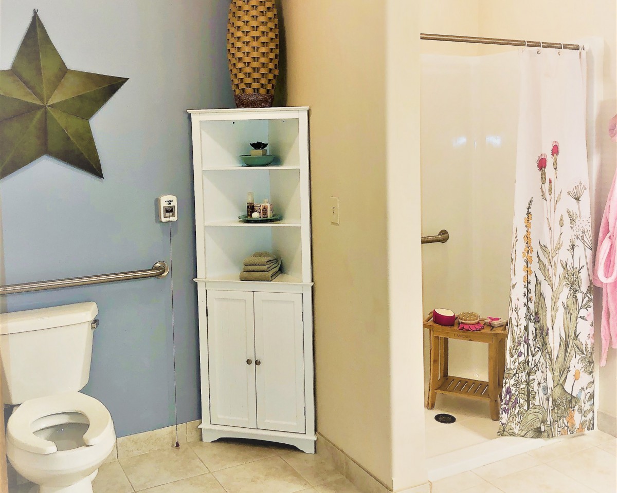 A modern bathroom with a shower, toilet, and a white corner cabinet for storage.