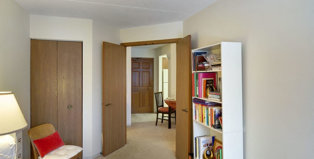 A cozy interior featuring an open doorway, a bookshelf filled with books, and a glimpse of the adjacent room with furniture.