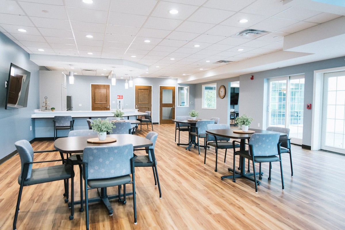 A modern, well-lit dining room with multiple tables and chairs arranged on a wooden floor.