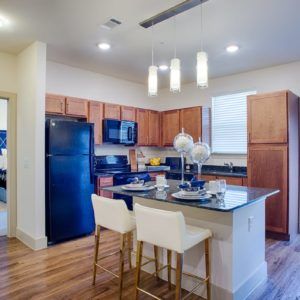 A modern kitchen featuring wood cabinets, a central island with bar stools, and various appliances.