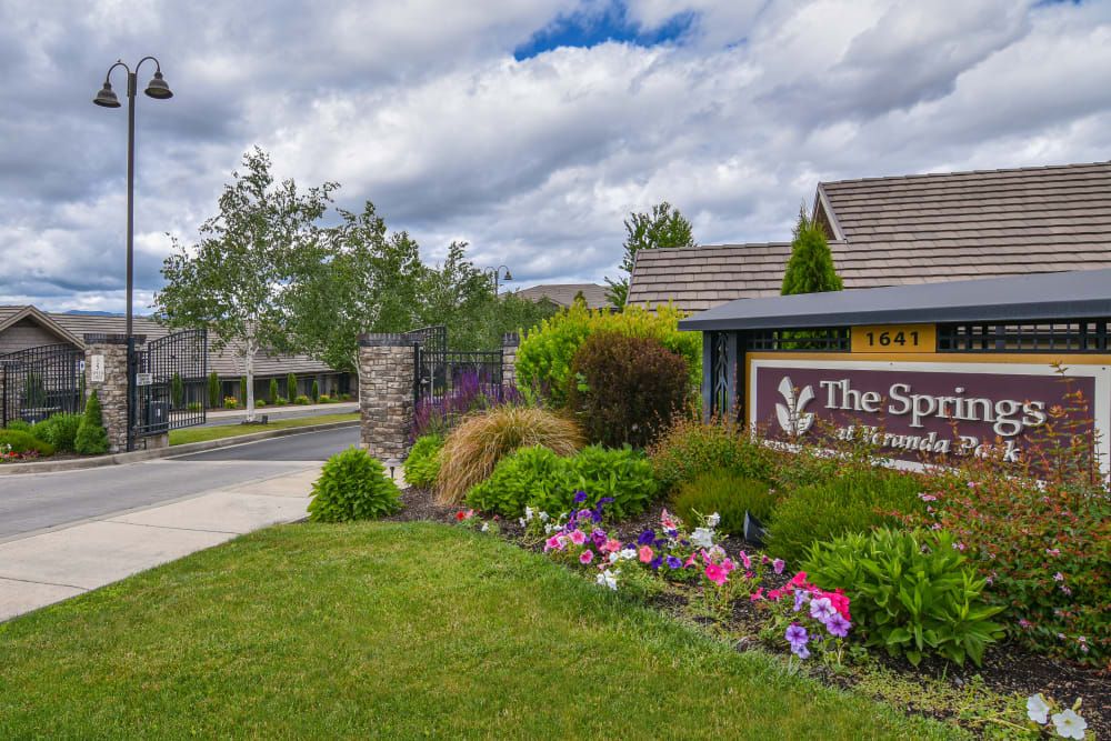 A beautifully landscaped entrance with a sign and vibrant flowers, set against a cloudy sky.