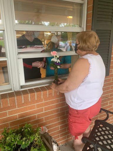A person handing a flower through a window, engaging with others inside.