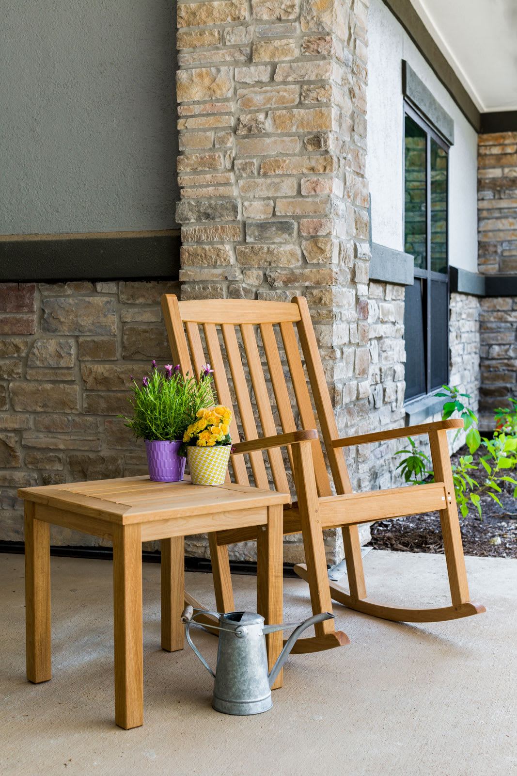 A wooden rocking chair and side table with potted plants on a porch.