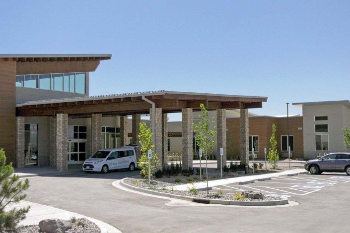 A modern building entrance with a car parked nearby on a sunny day.