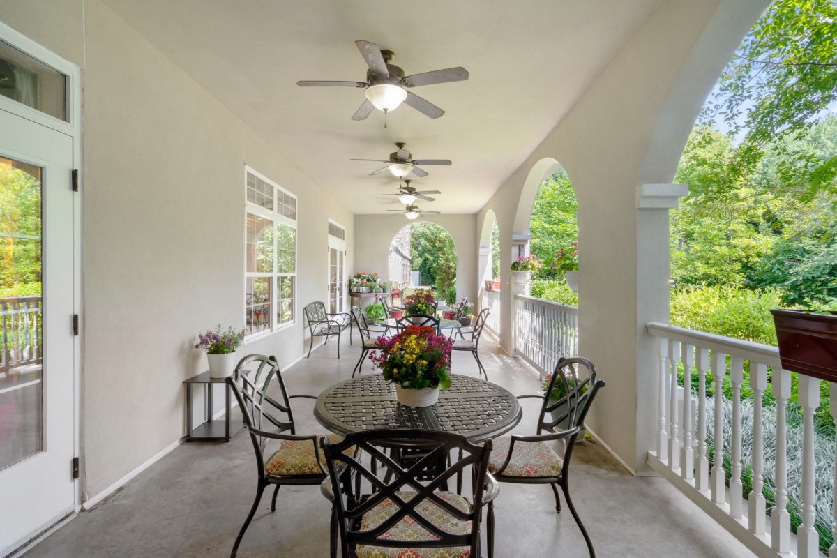 A spacious porch with comfortable seating, ceiling fans, and lush greenery.