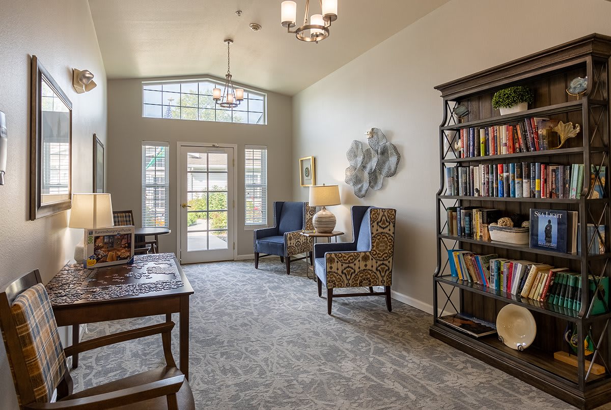 A cozy living room with elegant furniture and a tall bookshelf, featuring large windows that let in natural light.