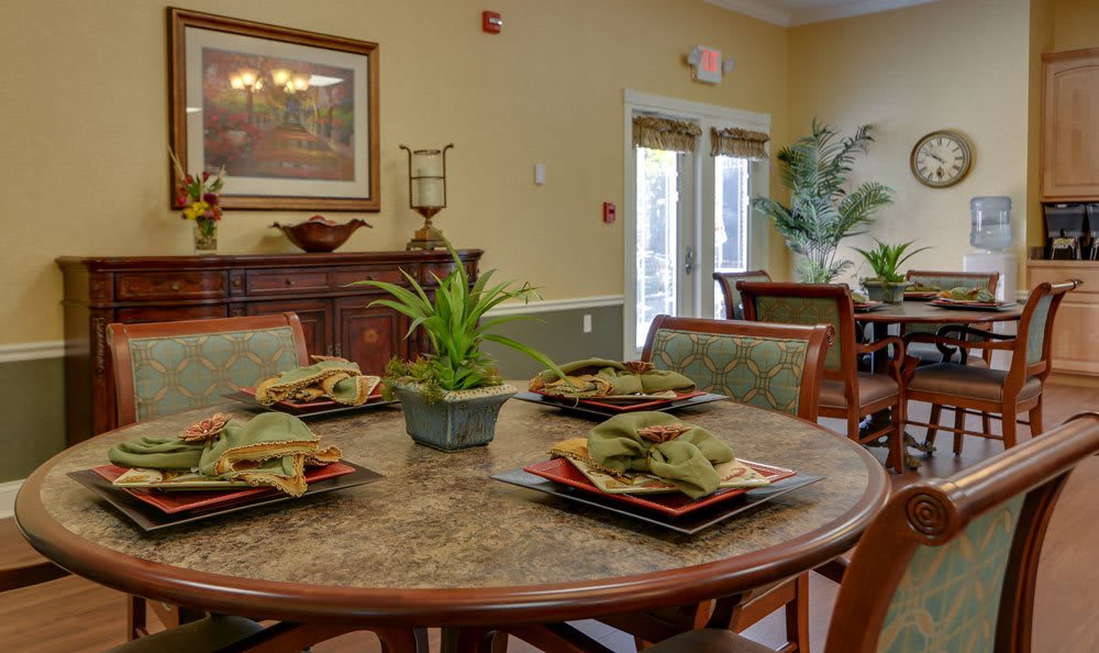 A cozy dining room with a round table set for four, featuring elegant dishware and a decorative plant centerpiece.