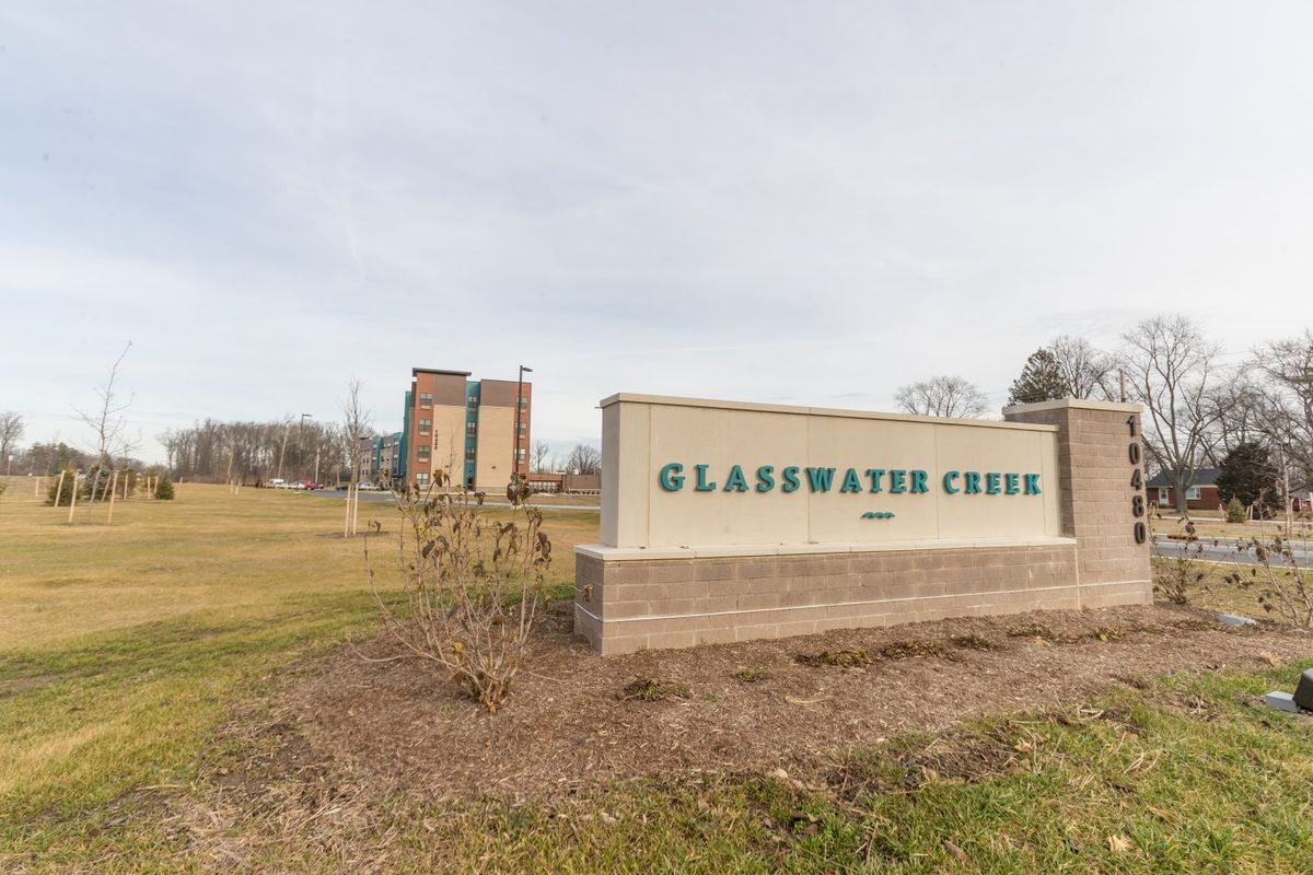 Entrance sign for Glasswater Creek with a building and landscaped area in the background.