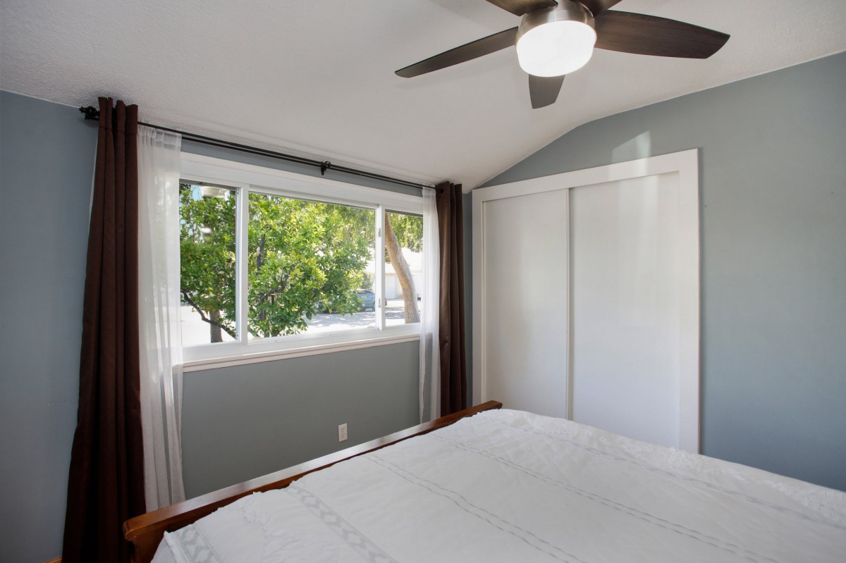 A minimalist modern bedroom with a large window, ceiling fan, and ample natural light.