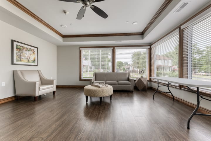 A modern living room with large windows, featuring a sofa, armchair, and wooden flooring.