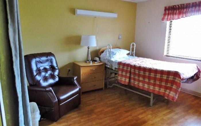 A nursing home room with a hospital bed, chair, and bedside table.