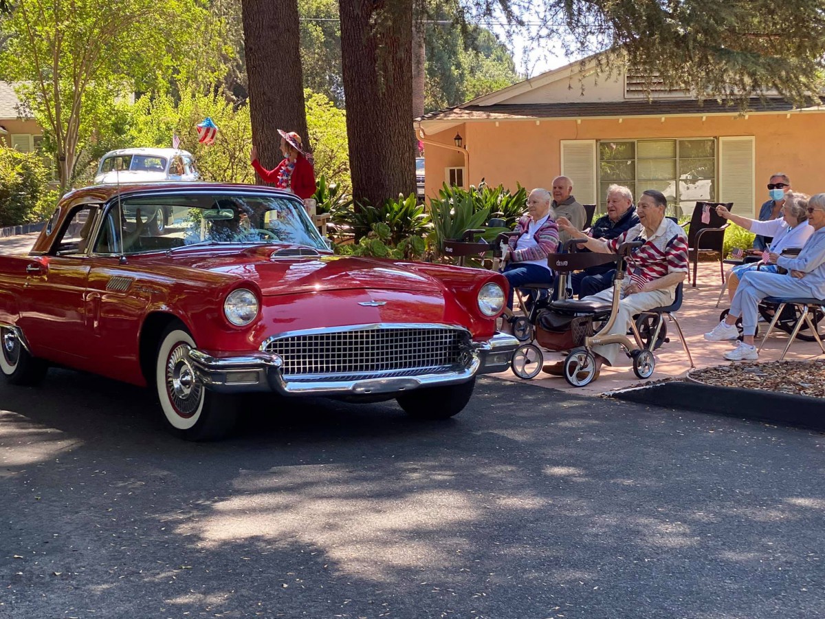 A group of people gather near a classic red car in an outdoor setting.