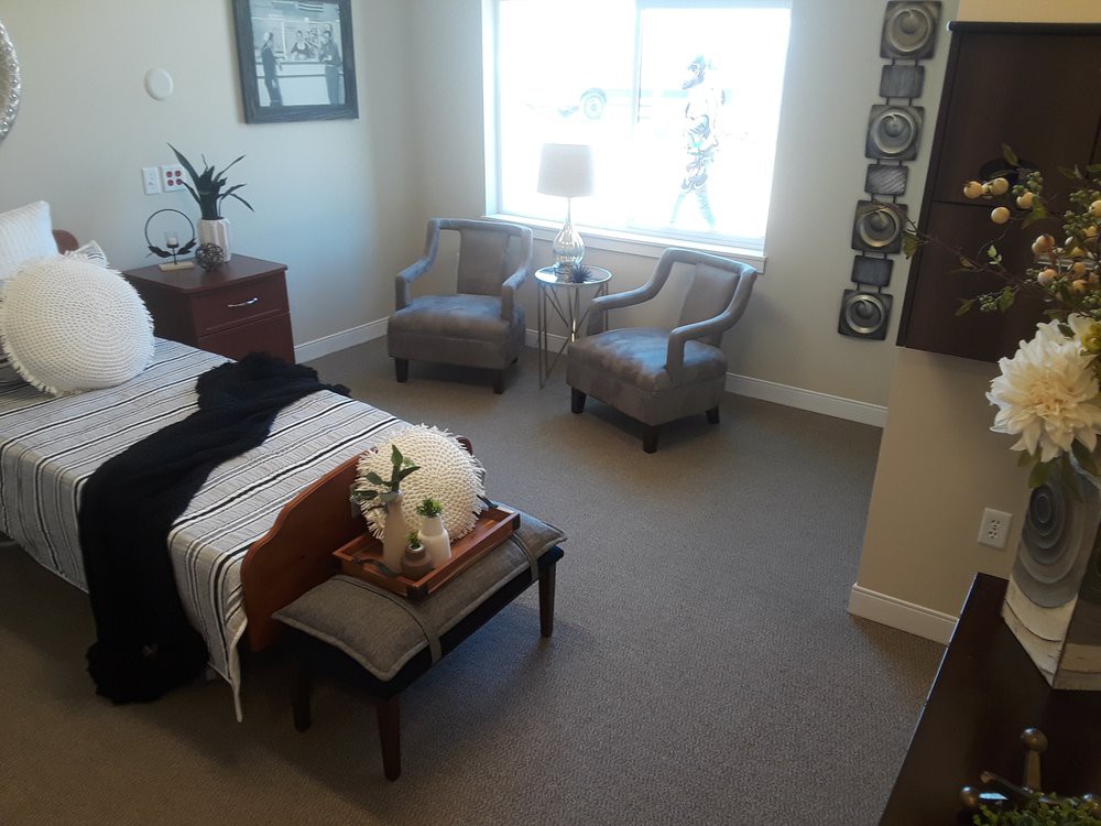 A cozy bedroom featuring a neatly made bed, two chairs by a window, and stylish decor.