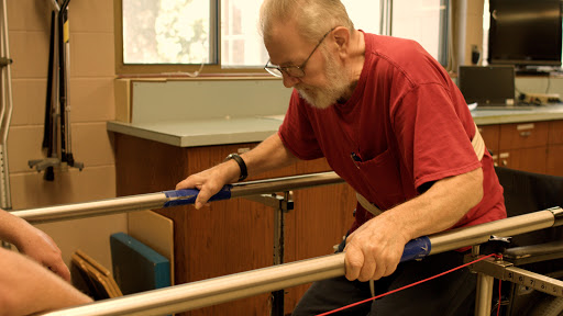 An elderly man using a parallel bar for physical therapy.