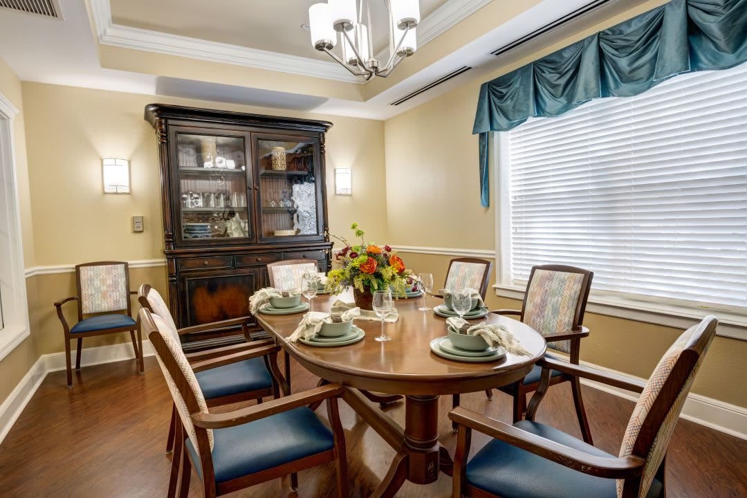 A traditional dining room with a wooden table set for four, surrounded by chairs and featuring a china cabinet against the wall.