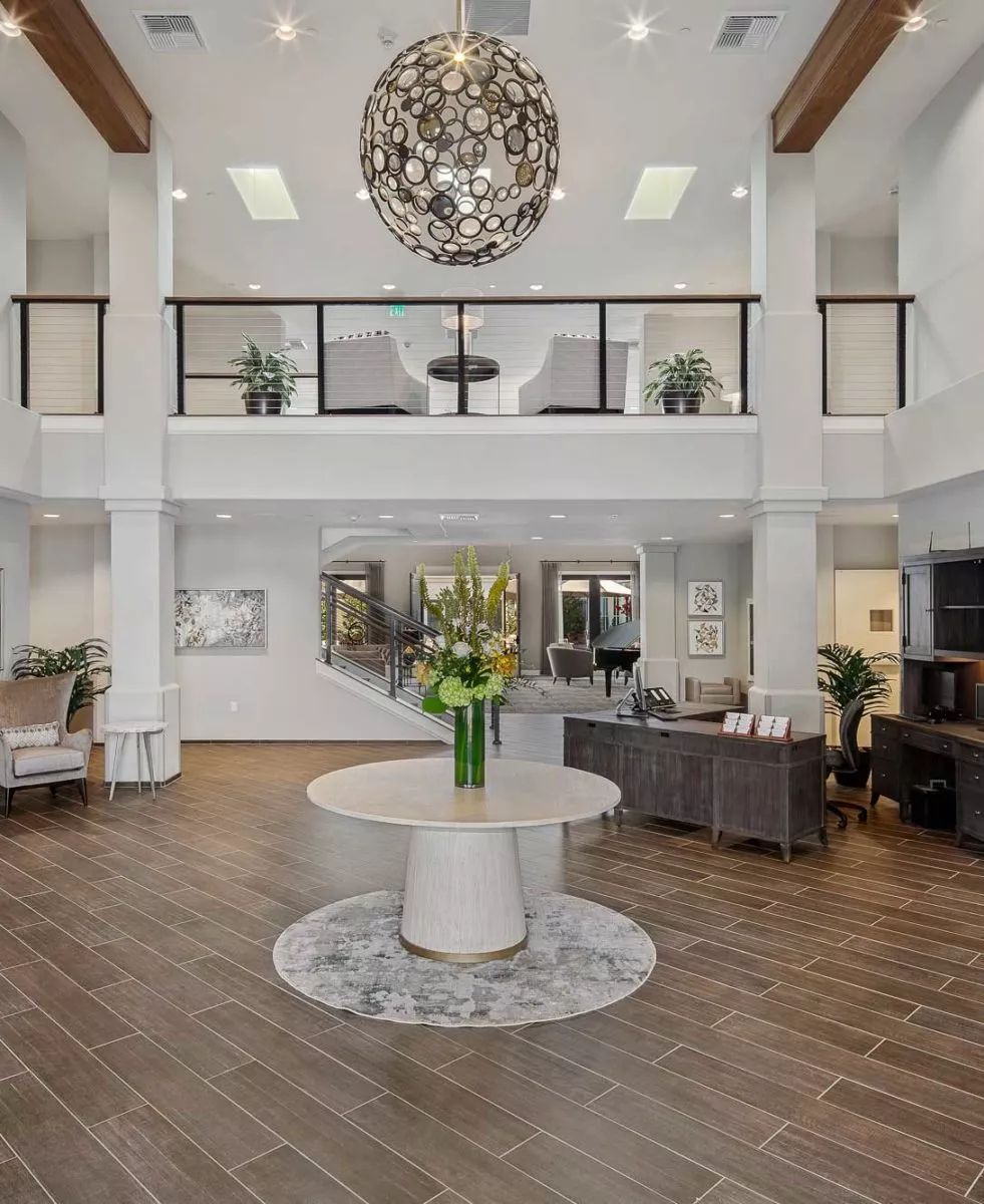 A modern lobby with a central table adorned with flowers, featuring elegant decor and a chandelier.