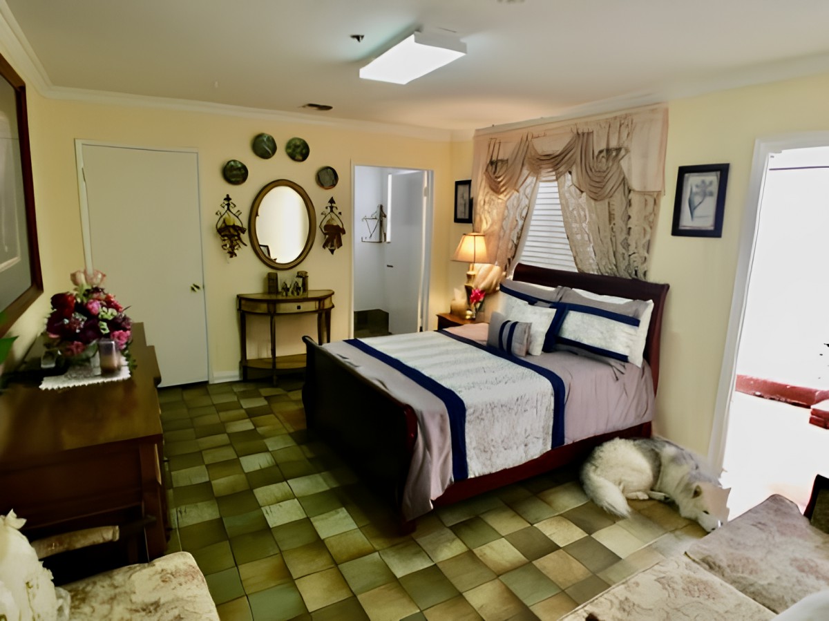 A cozy bedroom with a neatly made bed, decorative wall mirror, and warm lighting.