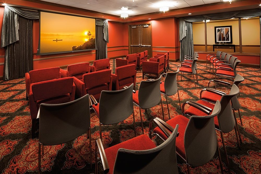 A conference room with neatly arranged chairs facing a large window, offering a sunset view.