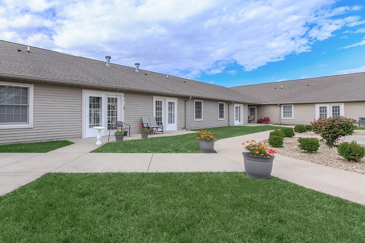 A well-maintained residential courtyard with green lawns and potted plants under a partly cloudy sky.