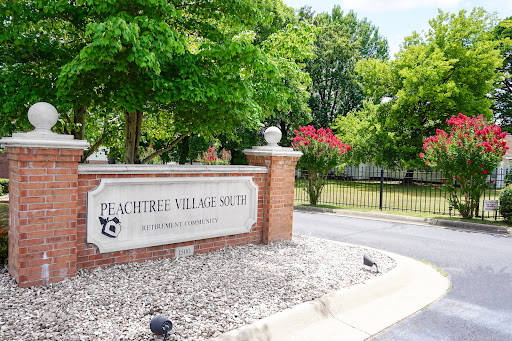 Entrance sign of Peachtree Village, surrounded by lush greenery.