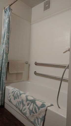A tidy bathroom featuring a shower tub combination with grab bars for safety.