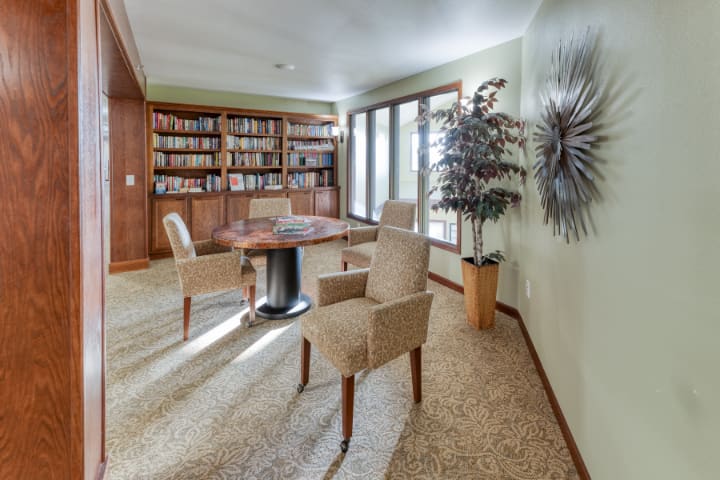 A cozy library room with bookshelves, a table, and chairs surrounded by natural light.