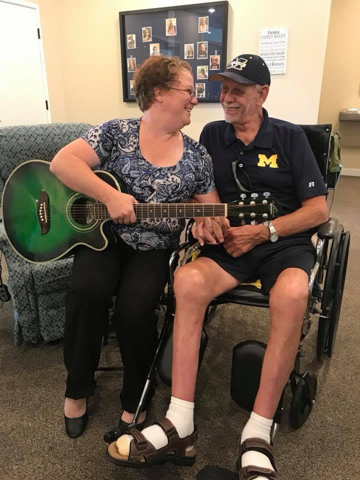 A smiling couple shares a moment, with one holding a guitar and the other sitting in a wheelchair.