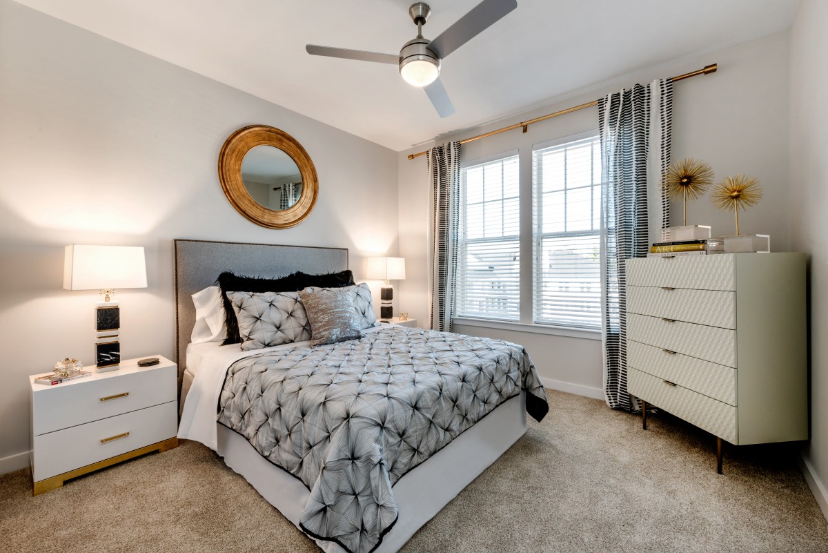 A modern bedroom with a double bed, decorative mirror, ceiling fan, and stylish furnishings.