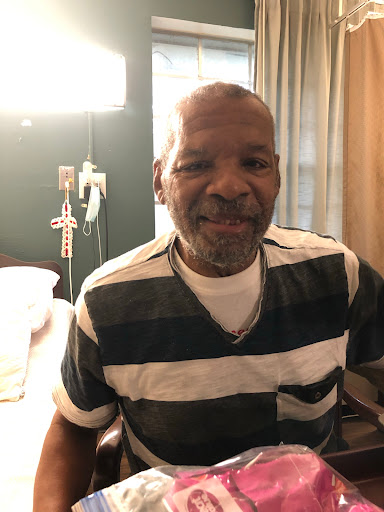 A man wearing striped clothing smiles while sitting in a hospital room.