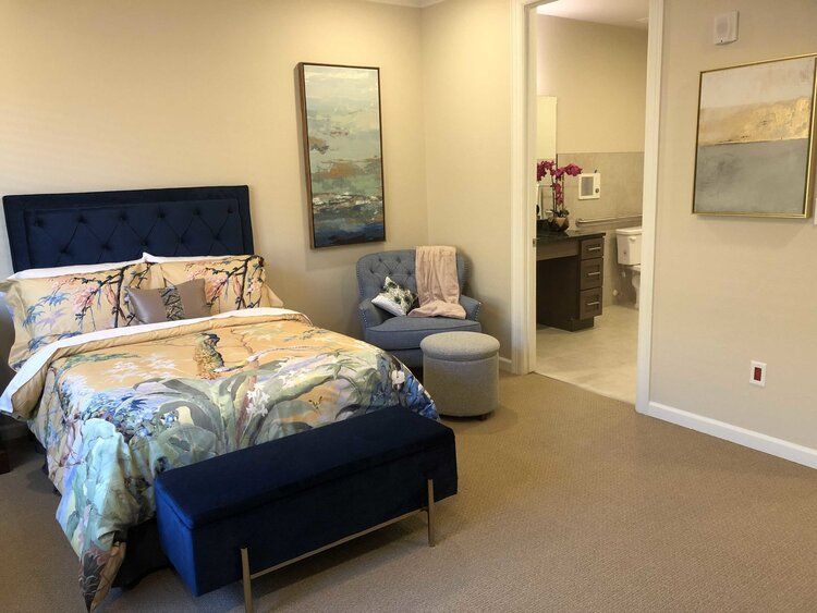 A modern bedroom with a comfortable bed, stylish armchair, and a view into the bathroom.