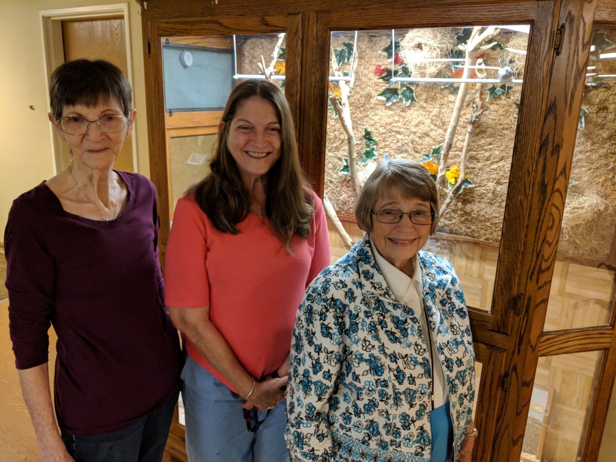 Three women smiling in an indoor setting with a decorative glass panel in the background.